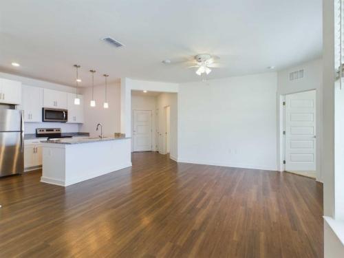 Apartments for rent in Ocala An empty modern apartment with hardwood flooring, an open kitchen with stainless steel appliances, granite countertops, white cabinetry, ceiling fan, and multiple doors. Aurora St. Leon Apartments in Ocala 2150 NW 21st Avenue | Ocala, FL 34475 (352) 233-4133