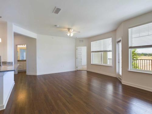 Apartments for rent in Ocala A spacious empty room with wooden floors, white walls, a ceiling fan, large windows, and a doorway leading to a bathroom or another room. Aurora St. Leon Apartments in Ocala 2150 NW 21st Avenue | Ocala, FL 34475 (352) 233-4133