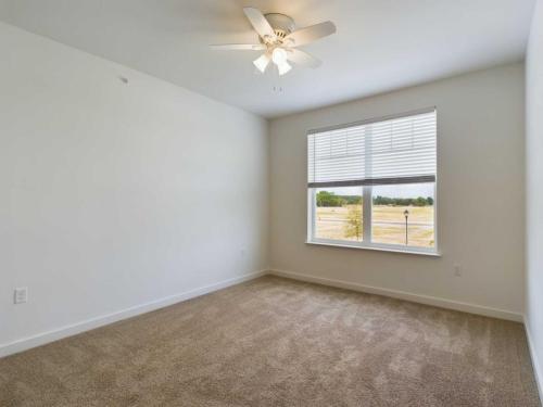 Apartments for rent in Ocala An empty room with beige carpet, a white ceiling fan, and a window with white blinds overlooking a grassy area. Walls are painted white. Aurora St. Leon Apartments in Ocala 2150 NW 21st Avenue | Ocala, FL 34475 (352) 233-4133