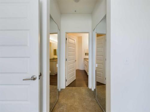 Apartments for rent in Ocala View of a hallway with carpeted flooring, mirrored closet doors on each side, and an open door leading to a bathroom with a double sink vanity. Aurora St. Leon Apartments in Ocala 2150 NW 21st Avenue | Ocala, FL 34475 (352) 233-4133