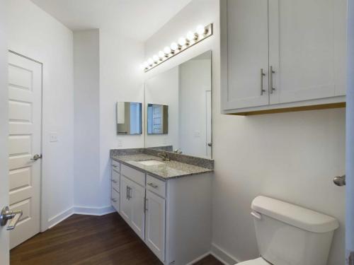 Apartments for rent in Ocala A modern bathroom with a double vanity, granite countertop, large mirror, white cabinets, and a toilet, featuring wooden flooring and white walls. Aurora St. Leon Apartments in Ocala 2150 NW 21st Avenue | Ocala, FL 34475 (352) 233-4133