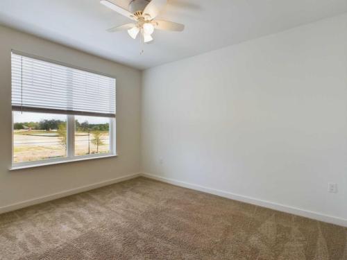 Apartments for rent in Ocala Empty room with beige carpet, a white ceiling fan, and a window with closed blinds. The walls are painted white and natural light enters from the window overlooking an outdoor landscape. Aurora St. Leon Apartments in Ocala 2150 NW 21st Avenue | Ocala, FL 34475 (352) 233-4133