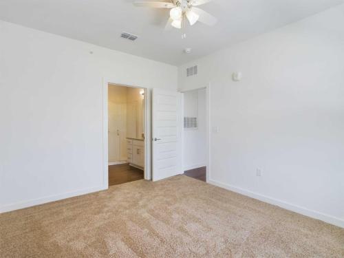 Apartments for rent in Ocala A bedroom with beige carpet, white walls, a ceiling fan with lights, and an open door leading to a bathroom. Aurora St. Leon Apartments in Ocala 2150 NW 21st Avenue | Ocala, FL 34475 (352) 233-4133