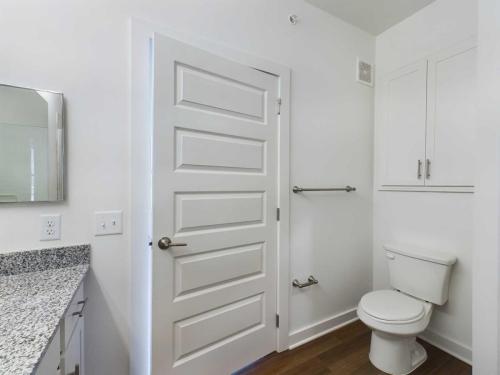 Apartments for rent in Ocala A clean, modern bathroom with white walls features a closed door, a granite countertop sink, a toilet, a towel bar, and a wall-mounted cabinet above the toilet. Aurora St. Leon Apartments in Ocala 2150 NW 21st Avenue | Ocala, FL 34475 (352) 233-4133