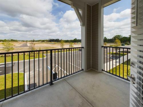 Apartments for rent in Ocala A balcony with a metal railing overlooks an empty parking lot and a grassy field under a partly cloudy sky. Aurora St. Leon Apartments in Ocala 2150 NW 21st Avenue | Ocala, FL 34475 (352) 233-4133