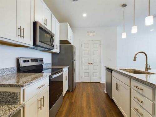 Apartments for rent in Ocala A modern kitchen features stainless steel appliances, granite countertops, white cabinets, a center island with a sink, and pendant lighting over the island. Aurora St. Leon Apartments in Ocala 2150 NW 21st Avenue | Ocala, FL 34475 (352) 233-4133