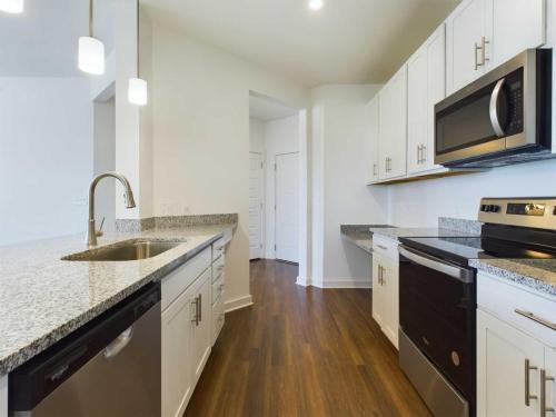 Apartments for rent in Ocala Modern kitchen with white cabinets, granite countertops, stainless steel appliances, and wood flooring. There's a sink with a faucet on the left side under hanging pendant lights. Aurora St. Leon Apartments in Ocala 2150 NW 21st Avenue | Ocala, FL 34475 (352) 233-4133