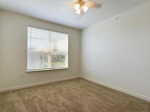 Apartments for rent in Ocala An empty room with beige carpet, a ceiling fan, and a window with closed blinds allowing some light in. Aurora St. Leon Apartments in Ocala 2150 NW 21st Avenue | Ocala, FL 34475 (352) 233-4133