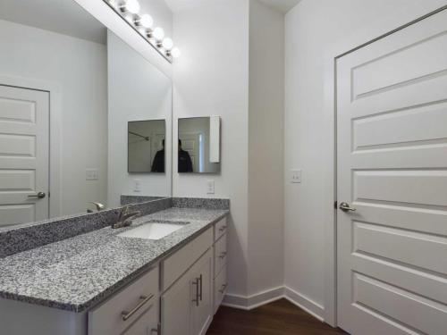 Apartments for rent in Ocala A modern bathroom features a granite countertop with a sink, double mirrors, white cabinets, and a closed white door. Four lights are mounted above the mirrors. Aurora St. Leon Apartments in Ocala 2150 NW 21st Avenue | Ocala, FL 34475 (352) 233-4133