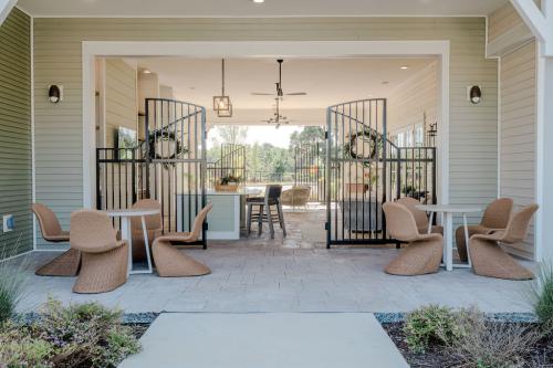 Apartments for rent in Ocala Outdoor patio with modern wicker chairs and round tables in front of a building with bifold metal gates, providing a view into a stylish indoor lounge area. Aurora St. Leon Apartments in Ocala 2150 NW 21st Avenue | Ocala, FL 34475 (352) 233-4133