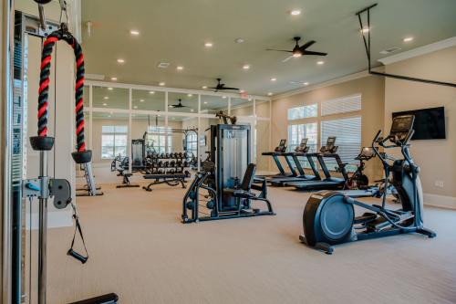 Apartments for rent in Ocala A modern gym with various fitness equipment including treadmills, ellipticals, weight machines, and a rack of dumbbells. The room has large mirrors and ceiling fans. Aurora St. Leon Apartments in Ocala 2150 NW 21st Avenue | Ocala, FL 34475 (352) 233-4133