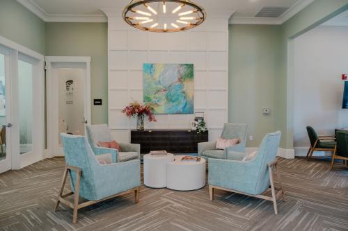 Apartments for rent in Ocala A modern waiting room with four light blue armchairs around two white circular tables, a colorful abstract painting on the wall, and a large chandelier overhead. There are flowers on a side table. Aurora St. Leon Apartments in Ocala 2150 NW 21st Avenue | Ocala, FL 34475 (352) 233-4133