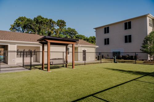 Apartments for rent in Ocala A fenced yard with artificial turf, featuring a wooden pergola and a bench, situated between a single-story building and a three-story building. Aurora St. Leon Apartments in Ocala 2150 NW 21st Avenue | Ocala, FL 34475 (352) 233-4133
